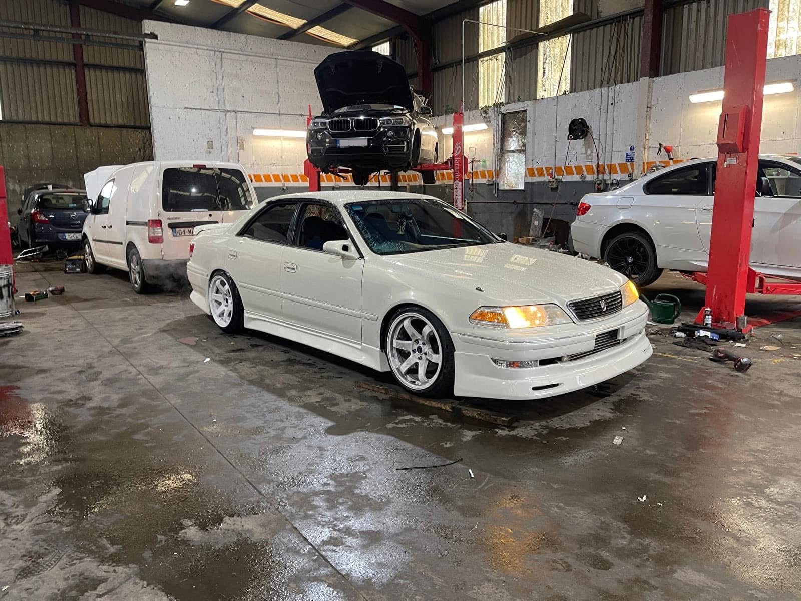 Modified white Toyota saloon on white wheels inside the workshop